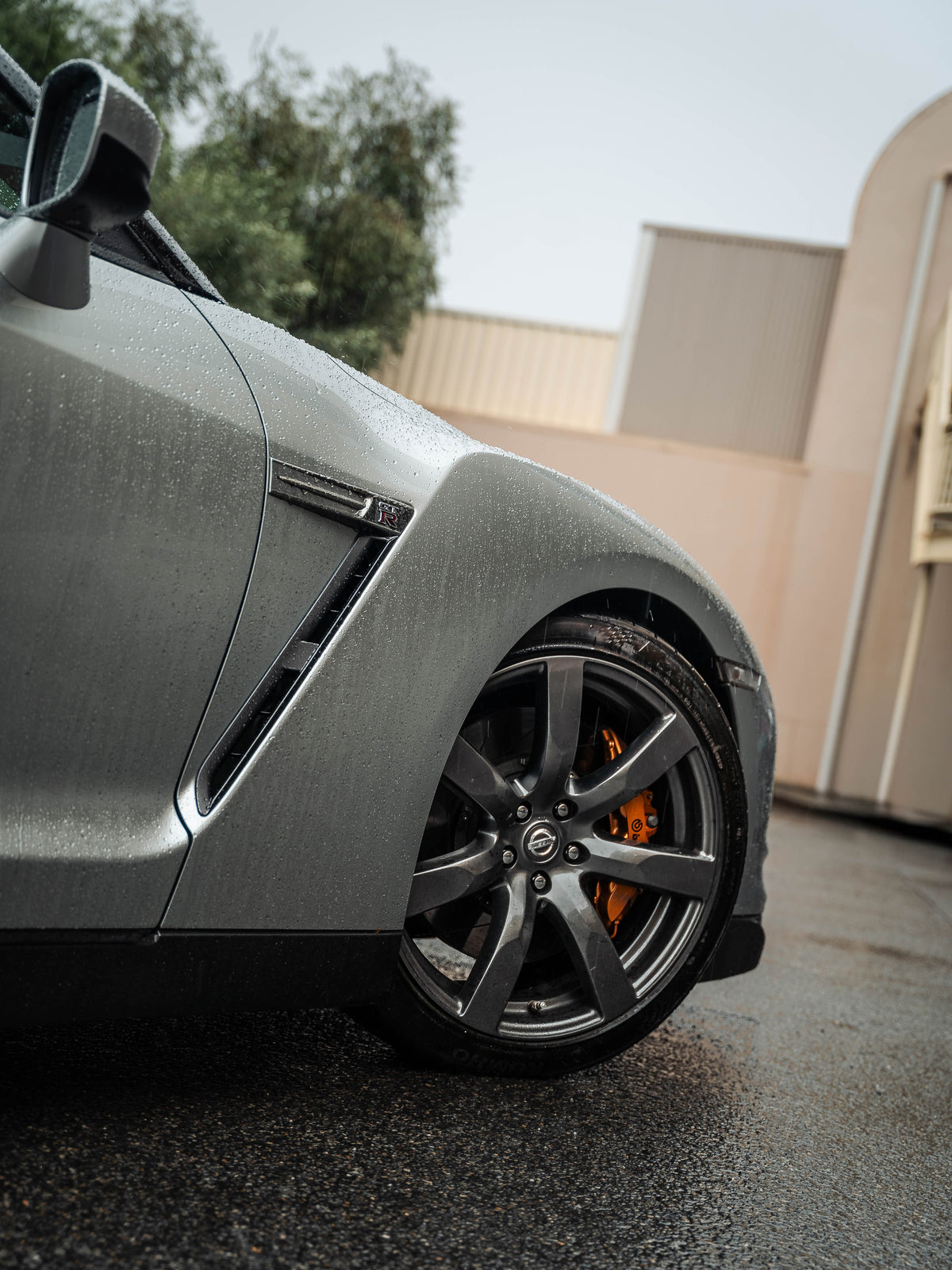 Grey sports car front wheel and quarter panel on wet asphalt