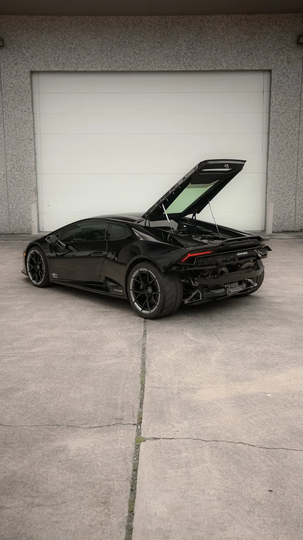 Black Lamborghini Huracan twin-turbo in front of an industrial garage door